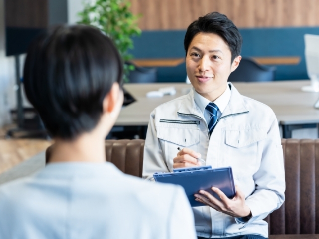 作業着の男性がバインダーを持ちながら女性と打ち合わせをする様子
