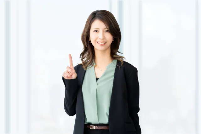 右手の人差し指を上げている笑顔のオフィスカジュアルの女性