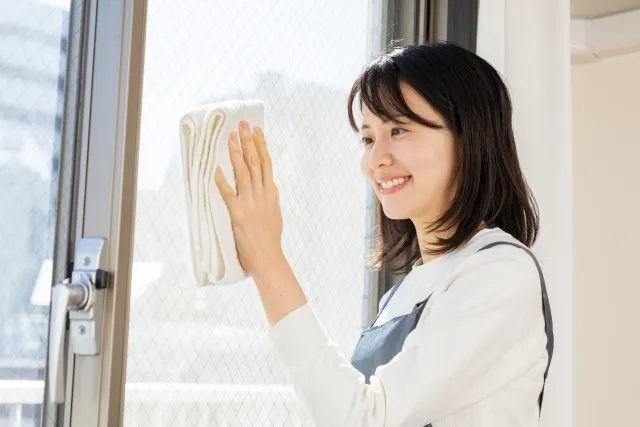 タオルで窓の清掃をしている笑顔のエプロンをした女性