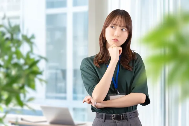 オフィスで半そでの女性が右手の拳を顎にあてて考えている