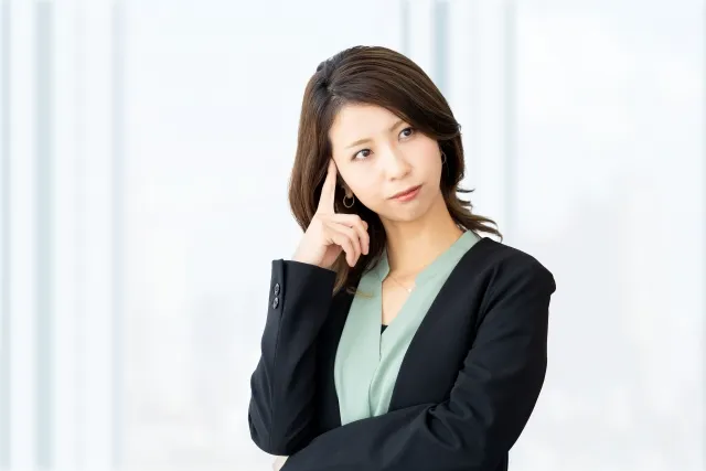 ジャケットを着た女性が右手の人差し指を頭に当てて考えている