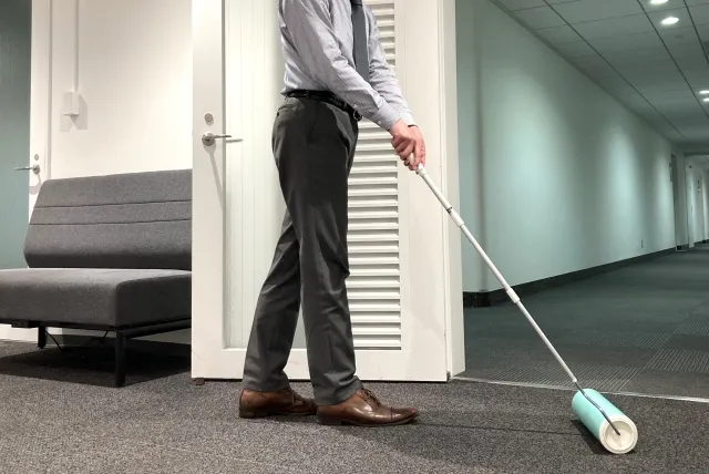 スーツを着た男性が柄の長い粘着カーペットクリーナーで社内のカーペットを掃除している