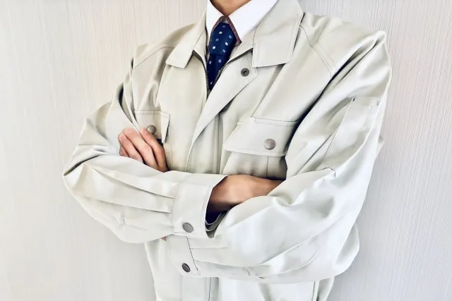 Yシャツにネクタイの上に作業着を着ている男性が腕組みをしている