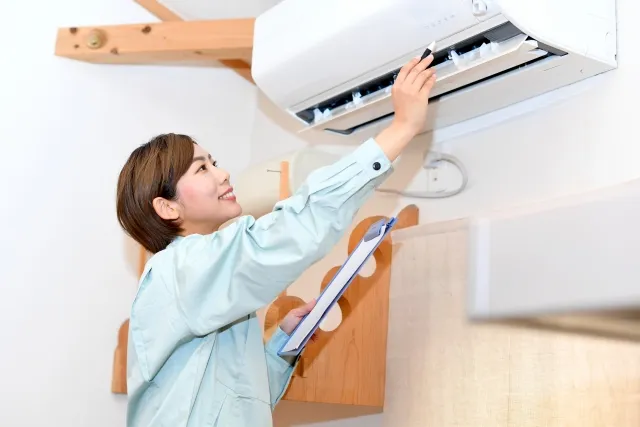家庭用エアコンを点検している作業着を着た女性作業員